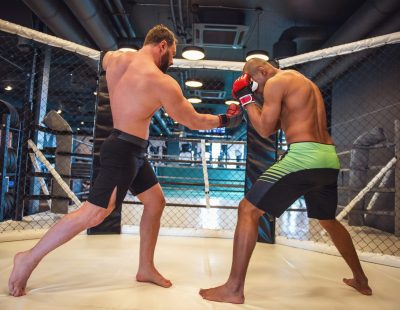 Two men in boxing gloves and shorts are fighting in cage